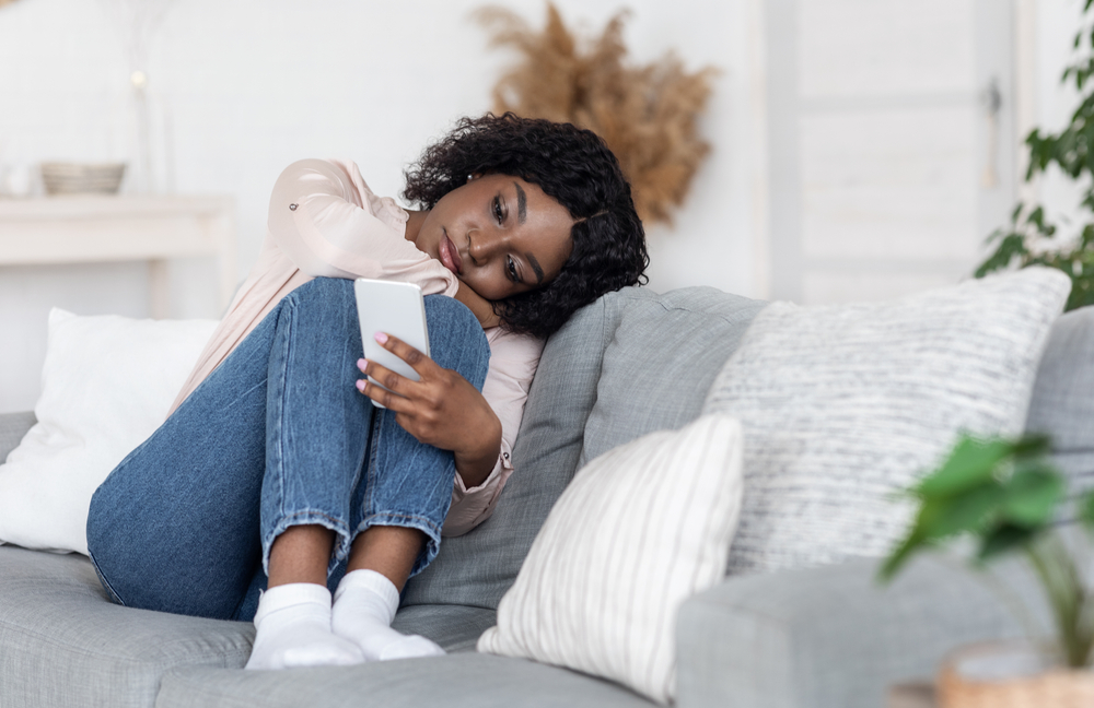 Loneliness.,Depressed,Black,Lady,Sitting,On,Couch,With,Smartphone,,Loking orbiting