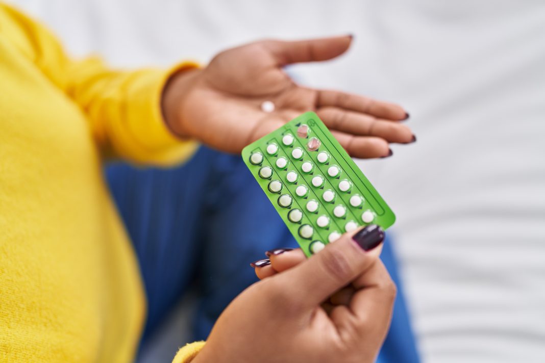 African,American,Woman,Holding,Birth,Control,Pills,Sitting,On,Bed anticonceptivos